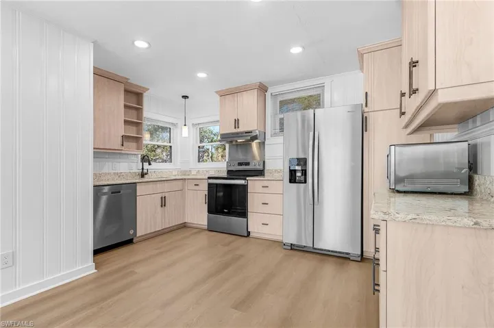 Kitchen featuring light brown cabinets, appliances with stainless steel finishes, light stone counters, hanging light fixtures, and recessed lighting