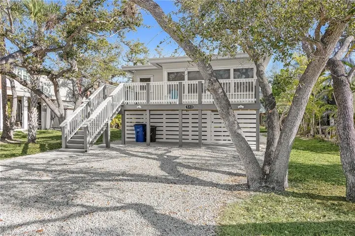 View of front facade featuring a wooden deck, stairs, gravel driveway, and an attached garage