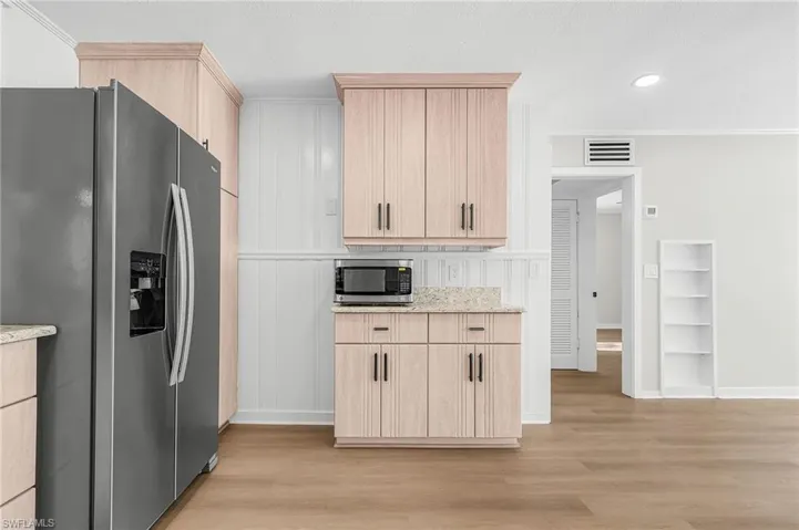 Kitchen with light brown cabinets, stainless steel appliances, light wood finished floors, light stone counters, and crown molding