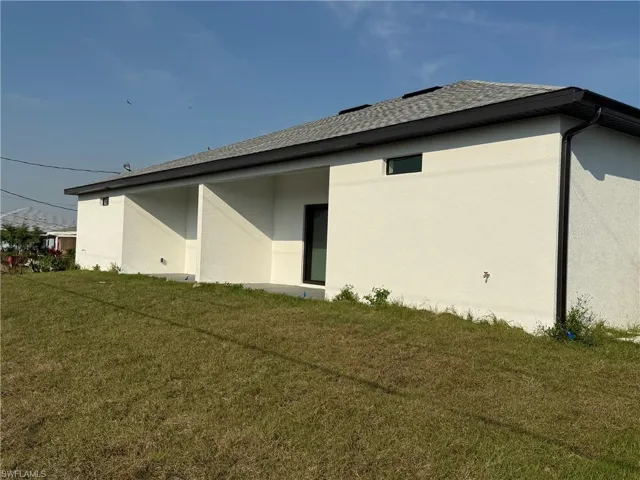 Rear view of property featuring a shingled roof, a yard, and stucco siding
