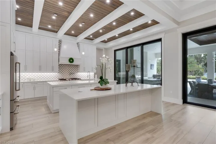 Kitchen featuring light stone countertops, white cabinets, tasteful backsplash, custom range hood, and wood finish floors