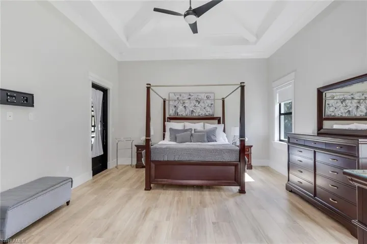 Bedroom with light wood-style floors, a ceiling fan, beam ceiling, and a high ceiling