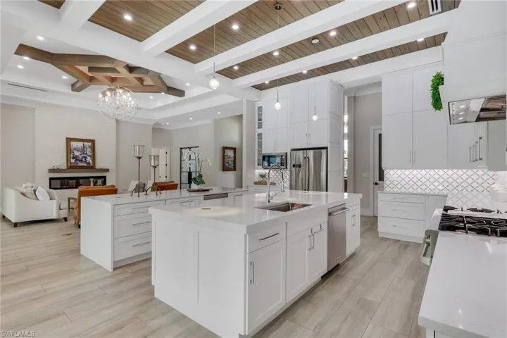 Kitchen with light stone countertops, open floor plan, white cabinetry, appliances with stainless steel finishes, and a wooden ceiling with exposed beams