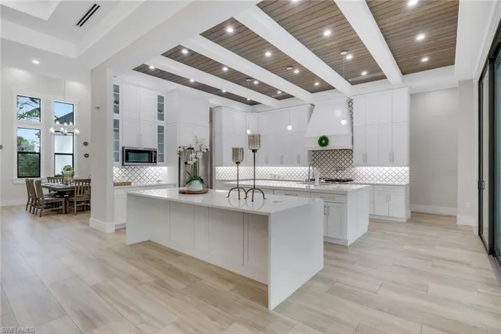 Kitchen featuring light stone countertops, white cabinets, custom range hood, backsplash, and a wooden ceiling with exposed beams