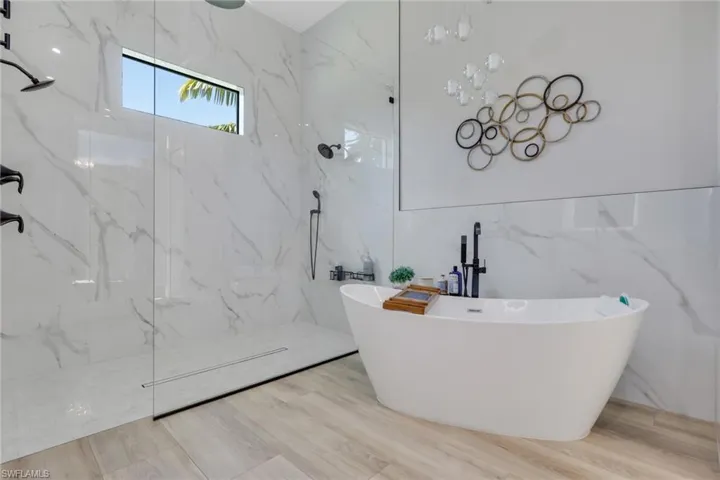 Full bathroom featuring a freestanding bath, tile walls, a marble finish shower, a wainscoted wall, and wood finished floors