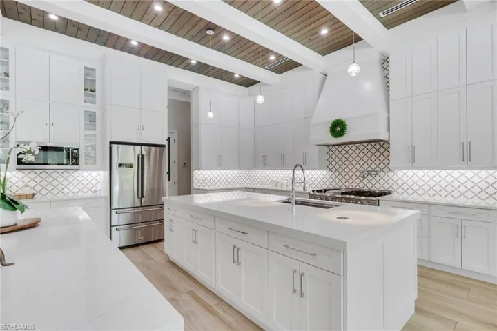 Kitchen with a kitchen island with sink, glass insert cabinets, a wood ceiling with exposed beams, stainless steel appliances, and pendant lighting