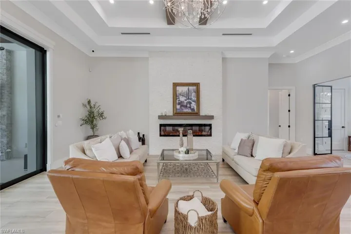 Living area featuring a fireplace, a raised ceiling, recessed lighting, and a chandelier