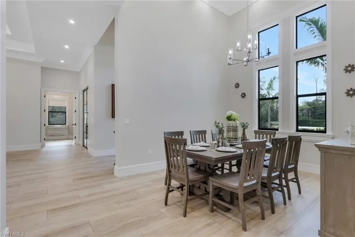 Dining room featuring healthy amount of natural light, a towering ceiling, light wood-type flooring, a chandelier, and recessed lighting