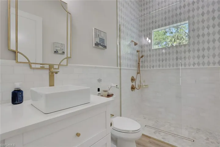 Bathroom featuring a walk in shower, vanity, tile walls, and wainscoting