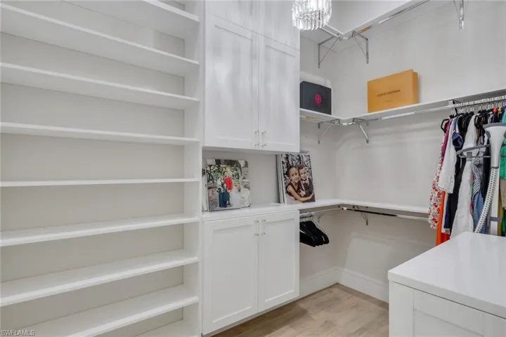 Walk in closet with light wood finished floors and a chandelier