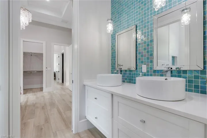 Bathroom with a chandelier, double vanity, a walk in closet, backsplash, and light wood finished floors