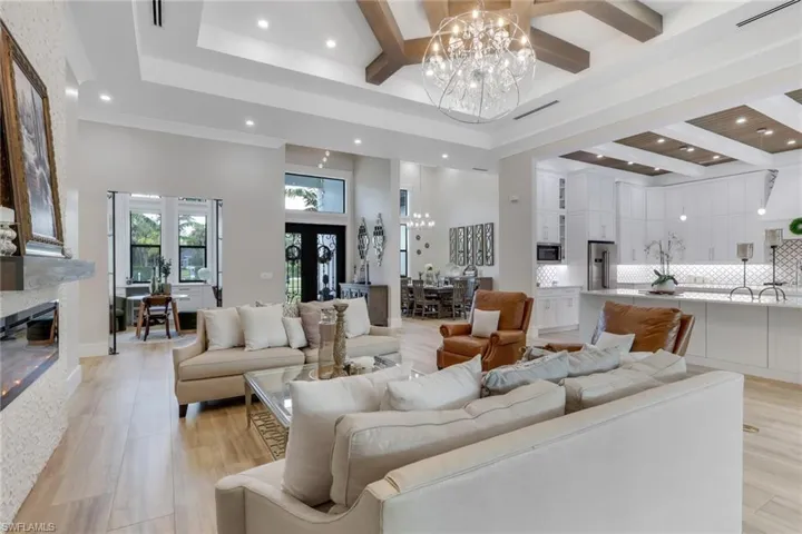 Living room with beam ceiling, a chandelier, a towering ceiling, coffered ceiling, and light wood finished floors