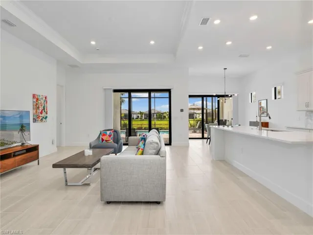 Open-concept living area featuring light-toned tile flooring, recessed lighting, and tray ceilings