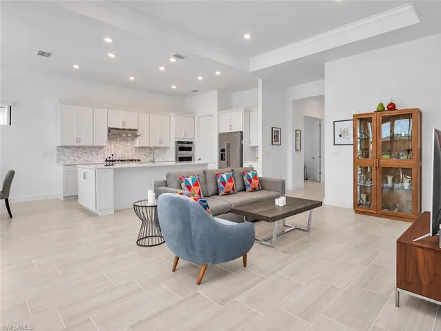 Open concept living area with light-toned tile flooring, recessed lighting, and a tray ceiling