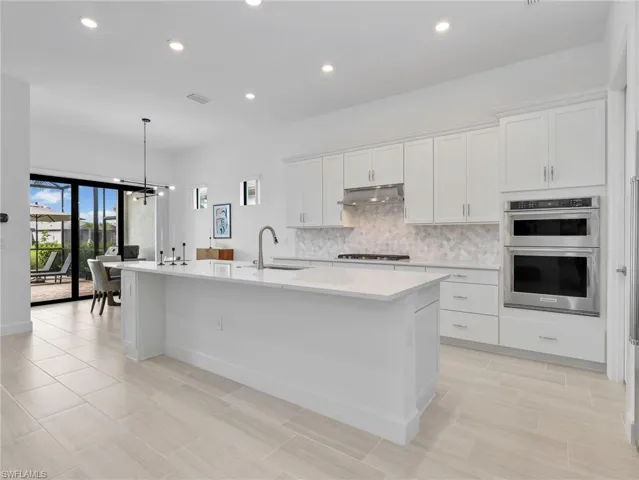 Expansive kitchen featuring a large central island, white cabinetry, stainless steel appliances, a tile backsplash, and light-toned tile flooring