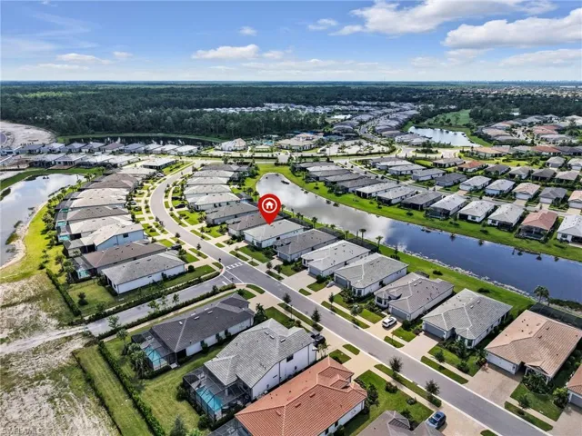 Aerial perspective of a residential community featuring multiple homes, street infrastructure, and water features