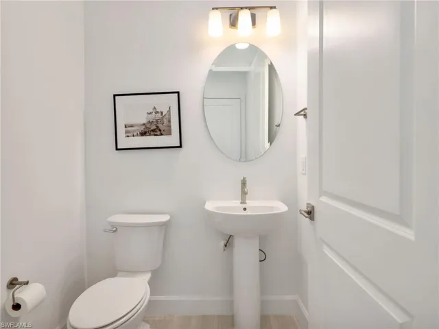 Hall Half Bathroom with White pedestal sink, a single-handle faucet, oval mirror, and a three-light vanity fixture