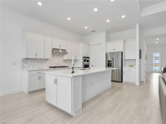 Contemporary kitchen with white cabinetry, stainless steel appliances, a center island with sink, and light-toned tile flooring