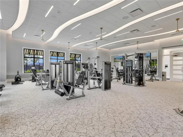 Fitness center featuring extensive exercise equipment, patterned carpet flooring, modern ceiling lighting, and multiple windows with awnings
