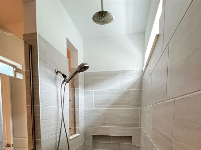 Primary Bathroom Shower featuring light-toned large format tile, a built-in shower niche, and a rain showerhead