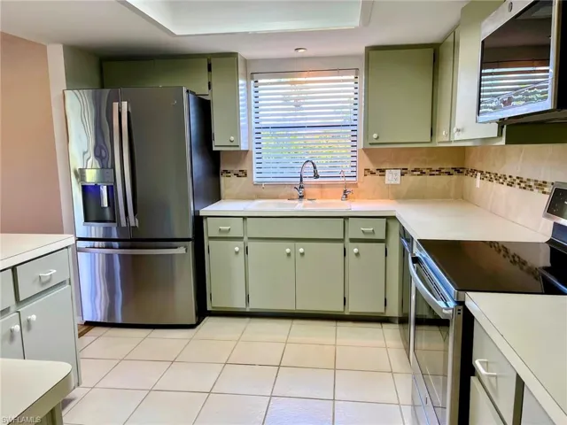 Kitchen featuring green cabinets, backsplash, appliances with stainless steel finishes, and sink