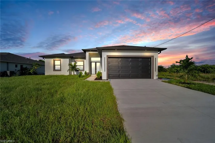 Prairie-style house featuring stucco siding, concrete driveway, an attached garage, and a lawn