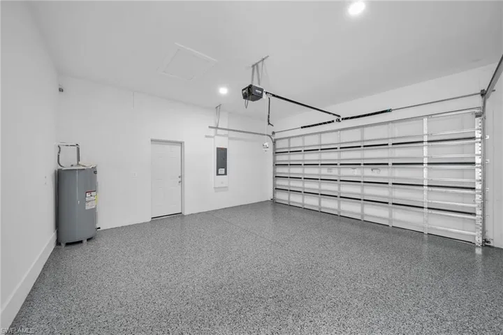 Garage with electric water heater, a garage door opener, recessed lighting, and electric panel