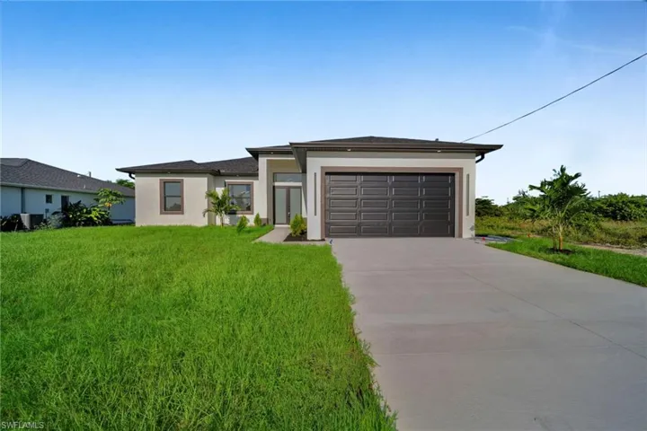 Prairie-style home featuring stucco siding, concrete driveway, an attached garage, and a front lawn