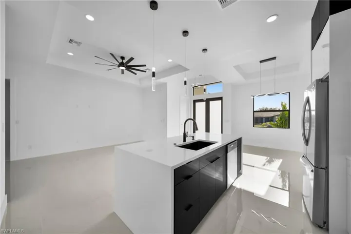 Kitchen with dark cabinetry, a raised ceiling, modern cabinets, decorative light fixtures, and appliances with stainless steel finishes