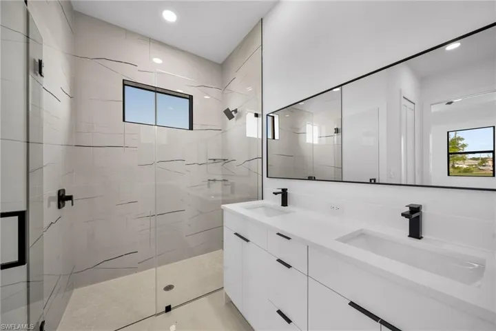 Full bathroom featuring a marble finish shower, double vanity, and recessed lighting