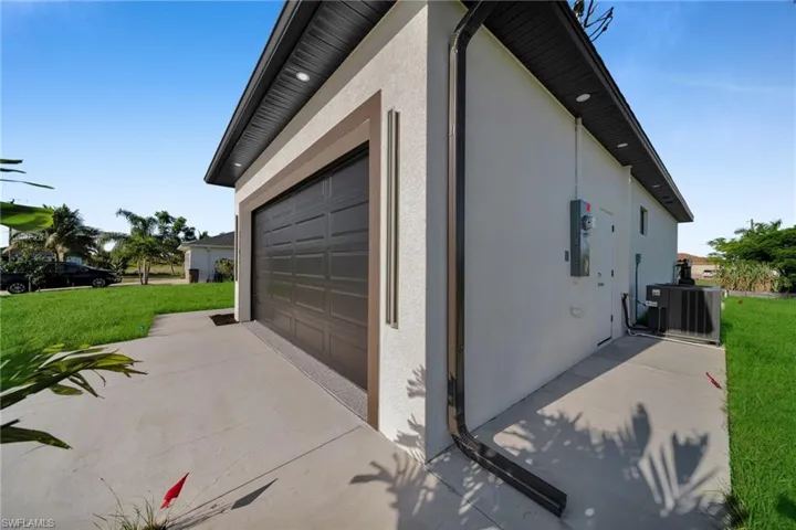 View of side of property with stucco siding, a lawn, concrete driveway, and a garage