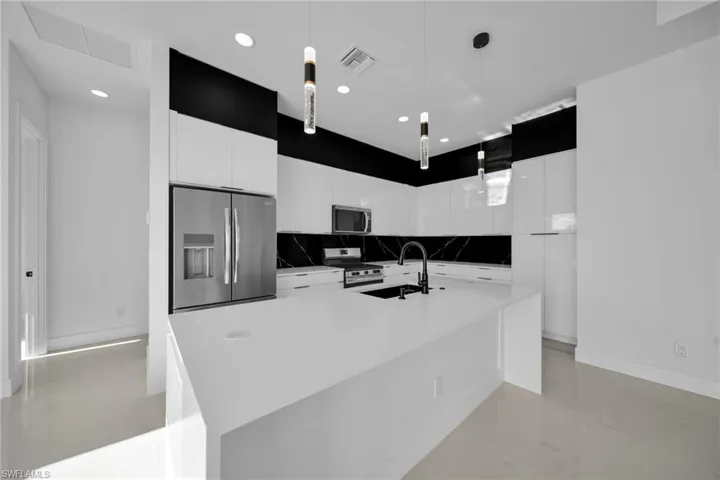 Kitchen featuring modern cabinets, white cabinets, stainless steel appliances, hanging light fixtures, and recessed lighting