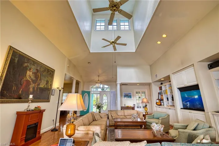 Living area with built in features, ornate columns, a high ceiling, a fireplace, and wood finished floors