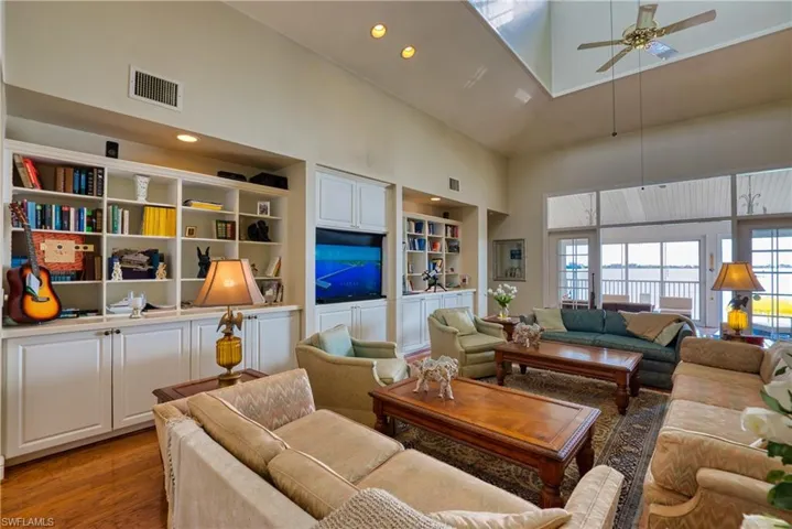 Living room featuring a high ceiling, a ceiling fan, wood finished floors, a skylight, and built in features