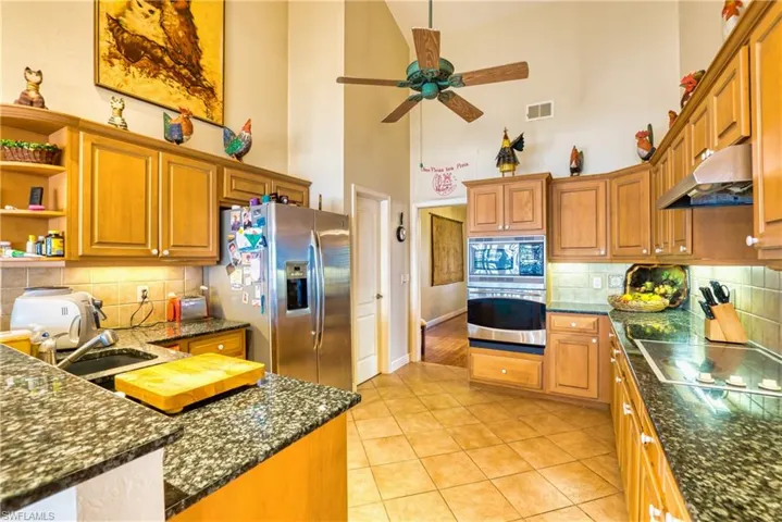 Kitchen featuring decorative backsplash, brown cabinetry, a high ceiling, stainless steel appliances, and under cabinet range hood