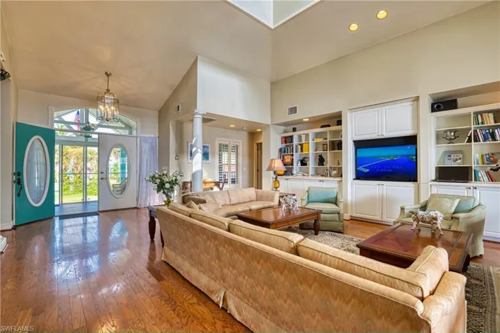 Living area with hardwood / wood-style floors, a towering ceiling, recessed lighting, a chandelier, and built in features