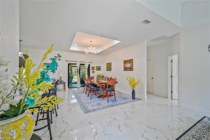 Spacious dining area featuring white tile flooring, a recessed ceiling with a chandelier, and sliding glass doors leading to an exterior space