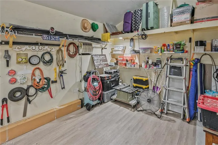 Utility space featuring wood-finish flooring, wall-mounted shelving, and an air conditioning unit