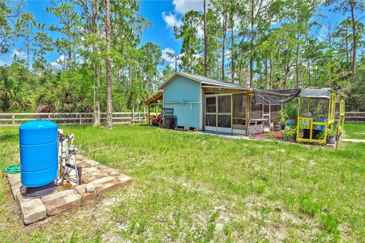 Expansive green space featuring a utility shed with a screened porch, a separate greenhouse structure, and a fenced perimeter