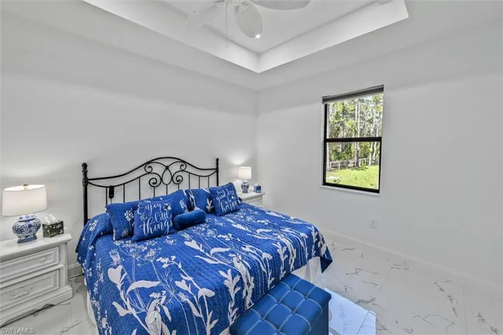 Spacious room featuring white walls, tray ceiling with a built-in ceiling fan, modern window with a black frame, and wood-finish flooring