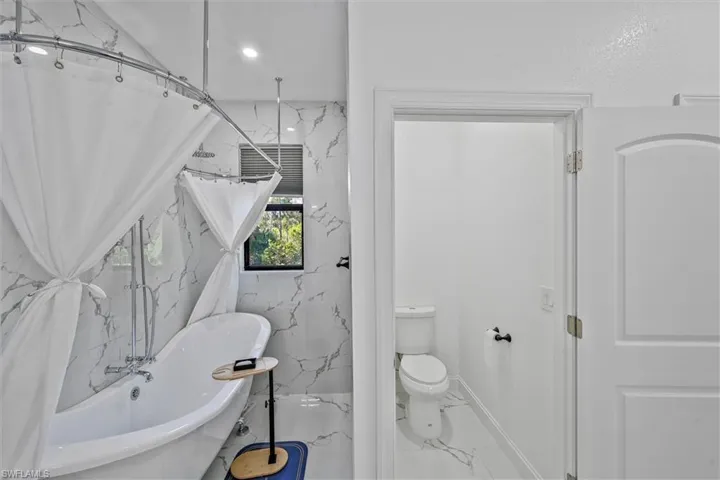 Freestanding soaking tub with a curved shower rod and ceiling-mounted showerhead, set against marble-look tile walls
