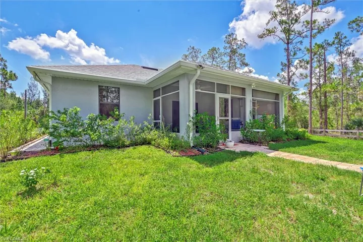 Rear exterior featuring a screened porch, a concrete patio, and a grass lawn with surrounding natural landscaping