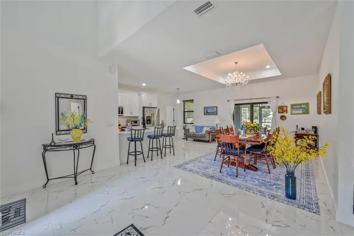 Spacious open-concept living area featuring white tile flooring, a tray ceiling with a chandelier, and a kitchen island with seating