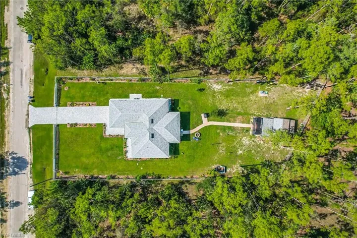 Expansive property featuring a grey shingle roof, a substantial paved driveway, electric / solar gate, a large green lawn, and two detached outbuildings