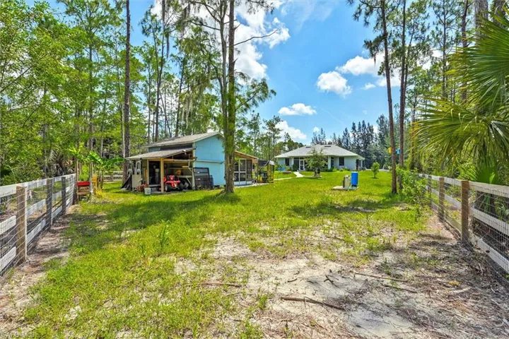 Expansive property featuring a wire and wood post fence, mature trees, a detached outbuilding with covered storage, and a single-story residence with a light-colored exterior and a screened porch
