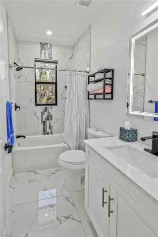 Bathroom featuring white and grey veined tile flooring and walls, white vanity with integrated sink, black fixtures, and a shower-tub combination