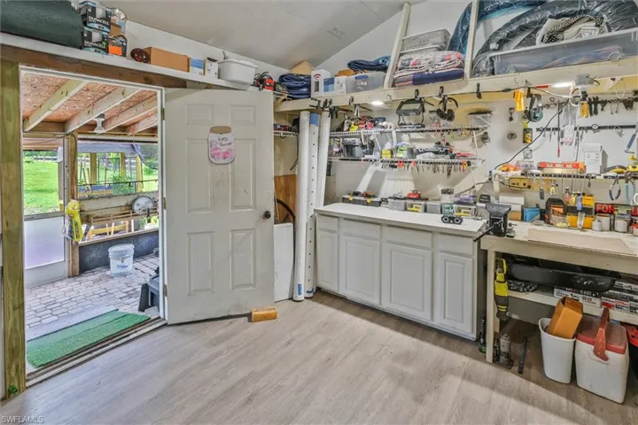 Workspace featuring wood-finish flooring, built-in cabinetry, an integrated workbench, and a covered patio area with a brick paver floor