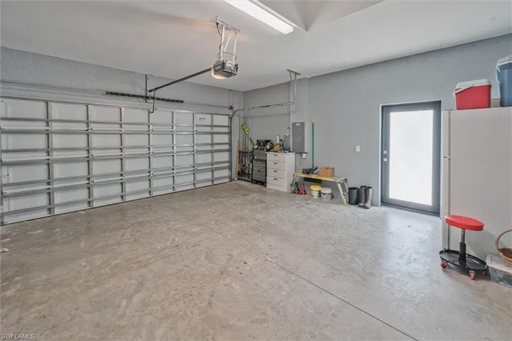Spacious garage featuring a concrete floor, a large sectional garage door with an automatic opener, a side entry door, and fluorescent overhead lighting