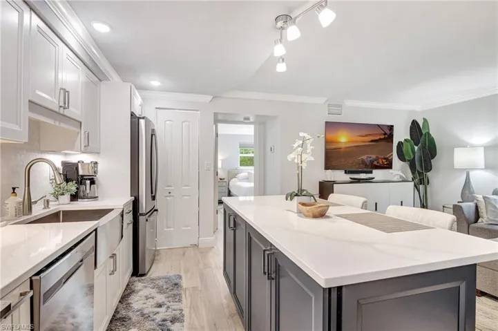 Kitchen featuring light wood-type flooring, a kitchen island, light stone counters, white cabinetry, and stainless steel appliances