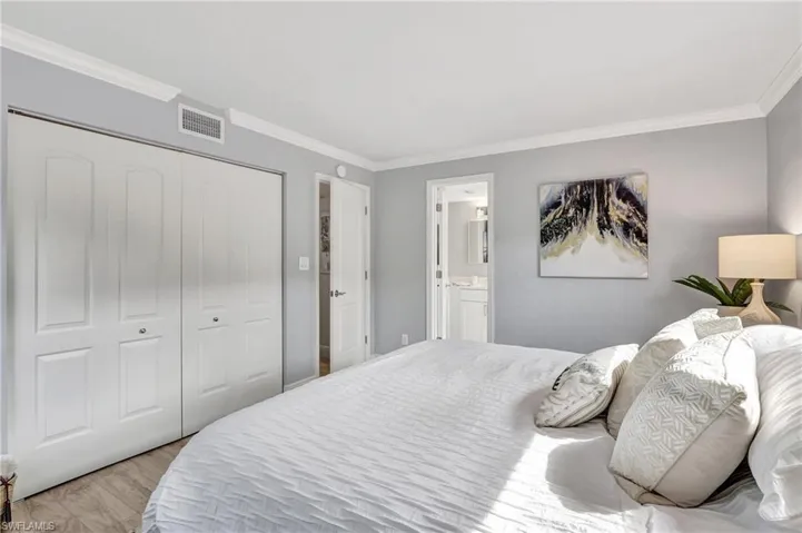 Bedroom with light hardwood / wood-style flooring, ensuite bath, a closet, and crown molding